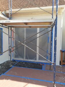 Scaffolding and a window prepped with plastic sheeting and tape for exterior wall work by Modern Wall Systems in Virginia Beach, VA.