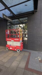 A red scissor lift positioned outside a commercial building for elevated repairs by DemoCraft Commercial Services in Everett, WA