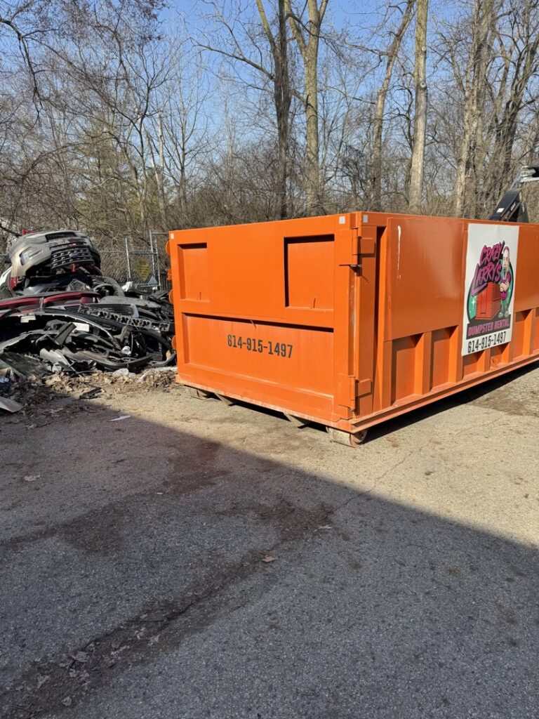A Crazy Larry's Dumpster Rental container positioned next to a large pile of scrap metal for removal in Columbus, OH.