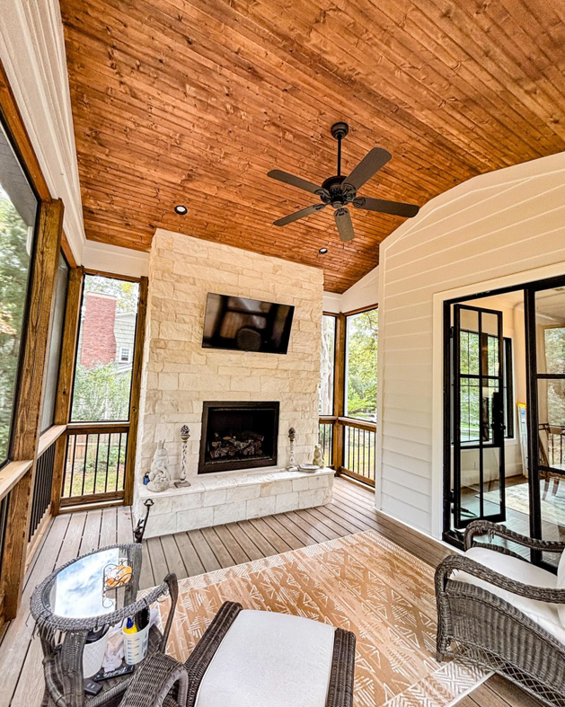 A beautifully designed screened-in porch with a stone fireplace and ceiling fan by Welcome Home Building Services in Winston-Salem, NC.