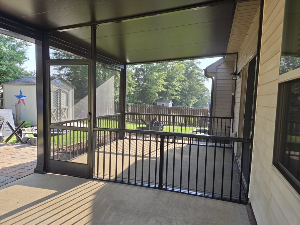 A newly built screened porch with black railings and a door leading to a concrete patio by Elite Xteriors NC in Cary, NC.