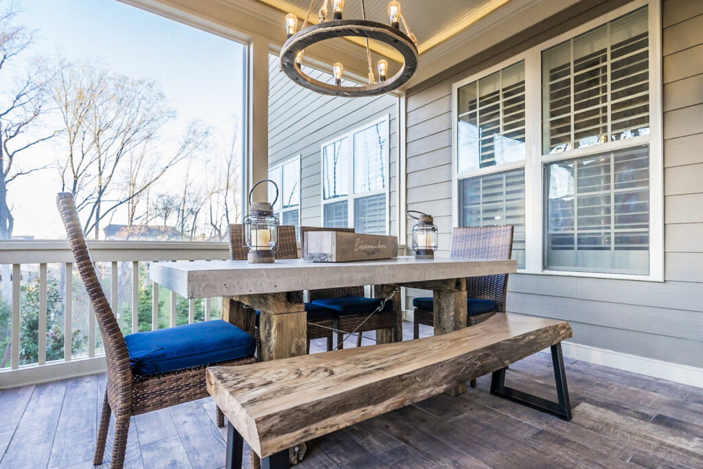 A beautifully furnished screened porch with a rustic chandelier and concrete-top table by Constructive Design Group in Raleigh, NC