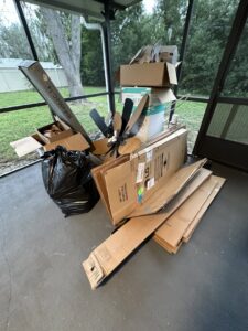 A screened-in porch cluttered with cardboard boxes, a ceiling fan, and a trash bag, ready for junk removal by Route Junk in Orlando, FL.