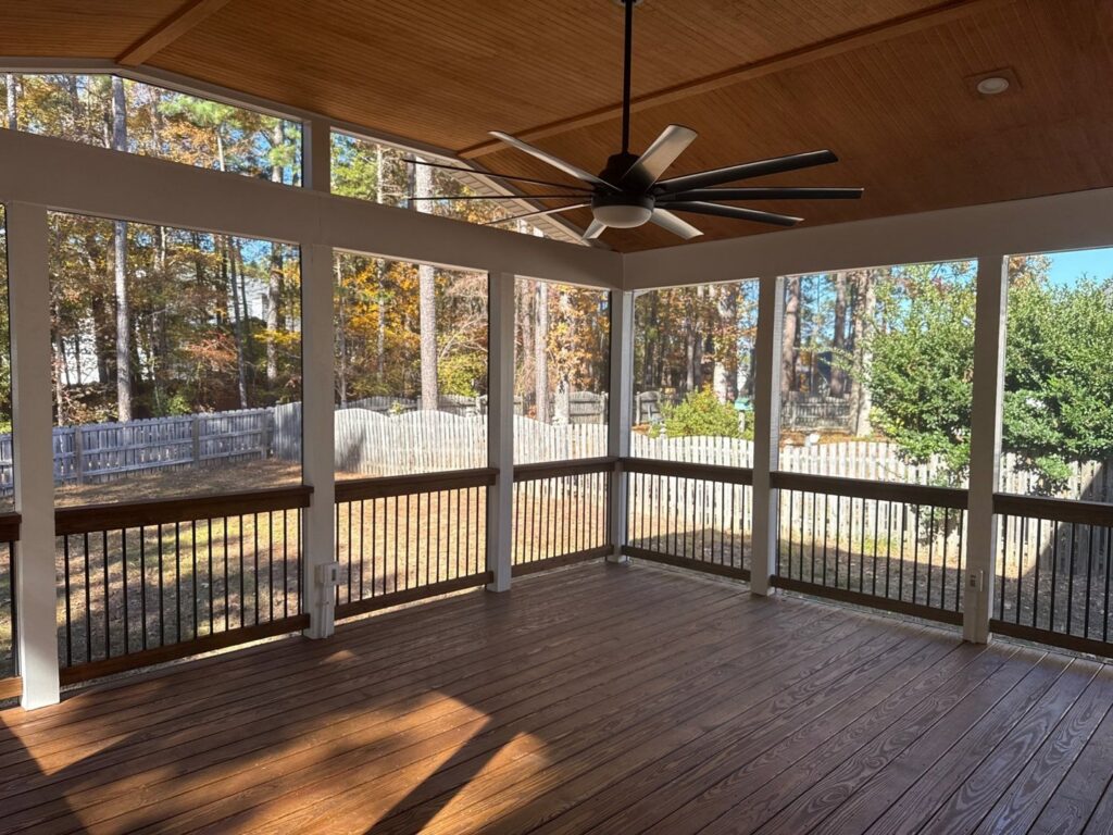 An interior view of a screened porch with a large ceiling fan and dark composite decking, built by Elite Xteriors NC in Cary, NC.