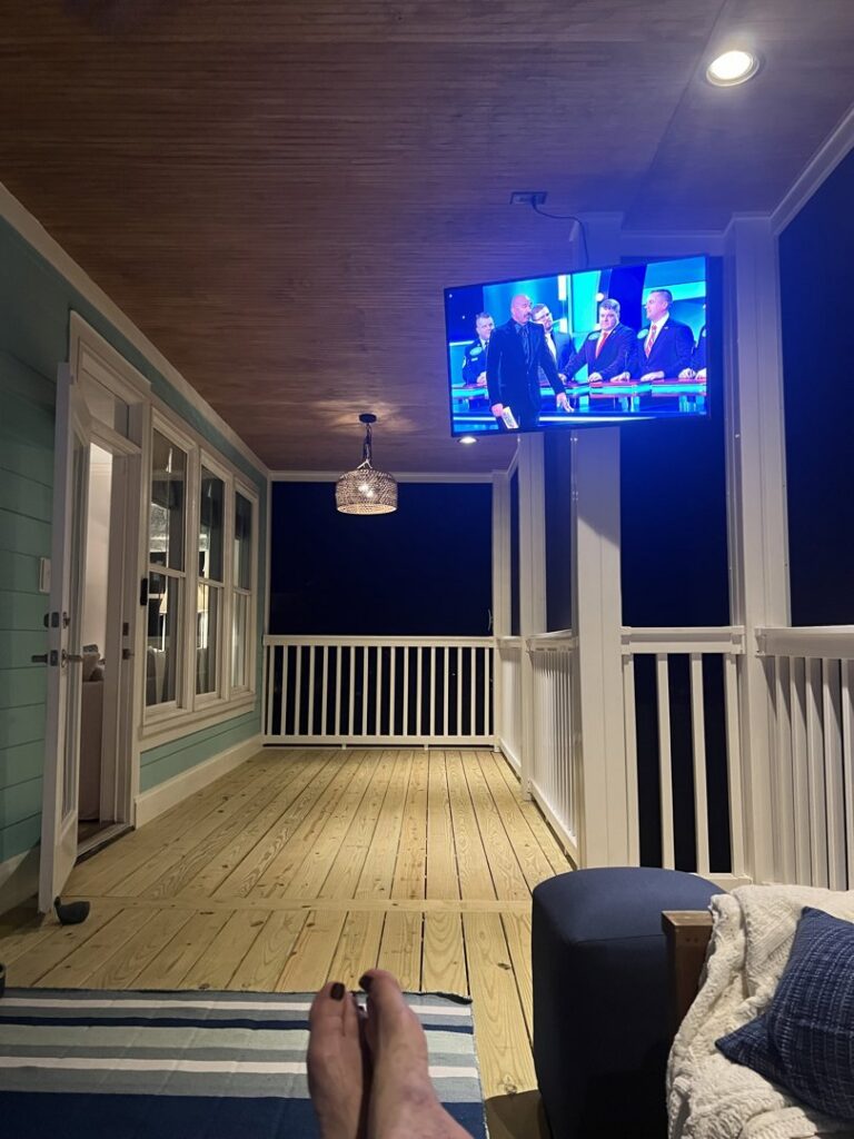 A cozy screened porch at night with a mounted TV and ambient lighting installed by Seaside Craftworks LLC in Wilmington, NC.