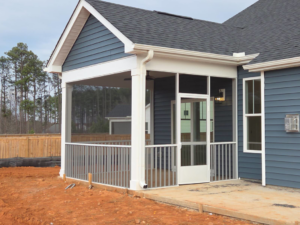 A newly built screened porch with white railings attached to a blue house by AccampoBros Home Solutions in Greenville, SC.