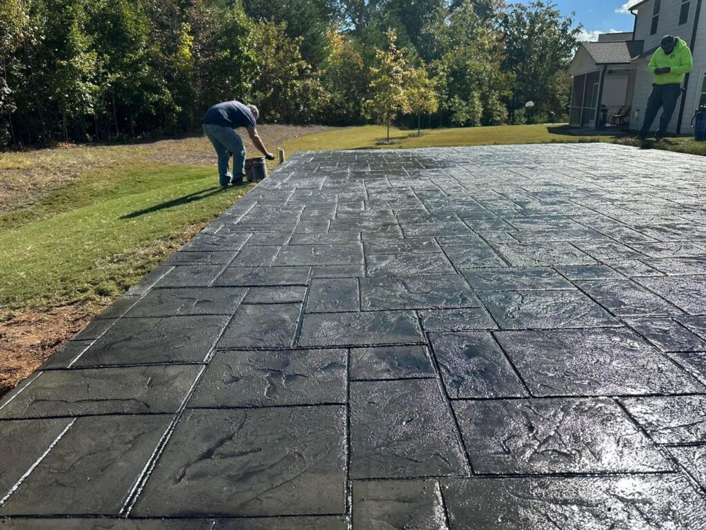Worker applying sealant to a newly installed stamped concrete patio by Solid Rock Builders in Rock Hill, SC.