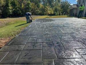 Worker applying sealant to a newly installed stamped concrete patio by Solid Rock Builders in Rock Hill, SC.