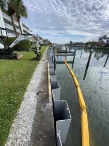 Seawall construction in progress with sheet piles being installed and an excavator on site by Bayside Concrete & Construction in Tampa, FL