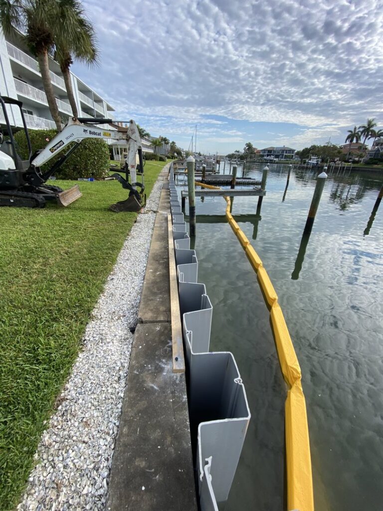 Seawall construction in progress with sheet piles being installed and an excavator on site by Bayside Concrete & Construction in Tampa, FL