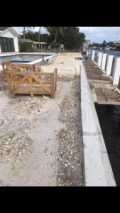 A construction site featuring a new concrete seawall, sand, and a pool area under development by Snapp Industries, Inc. in Miami, FL