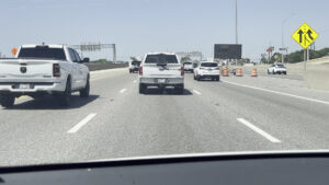 A SEDALCO Construction Services truck driving on a highway near road construction barrels in Fort Worth, TX.
