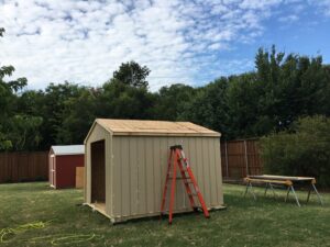 A new shed under construction in a backyard, with an orange ladder leaning against it, built by Texas Wounded Veterans Builders and Contractors in McKinney, TX.