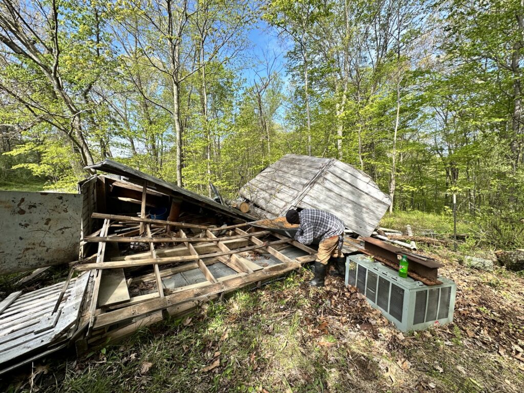 A worker dismantling a shed with debris scattered around, indicating a shed removal and junk cleanup job by Top Tier Waste Services LLC in Lancaster, OH