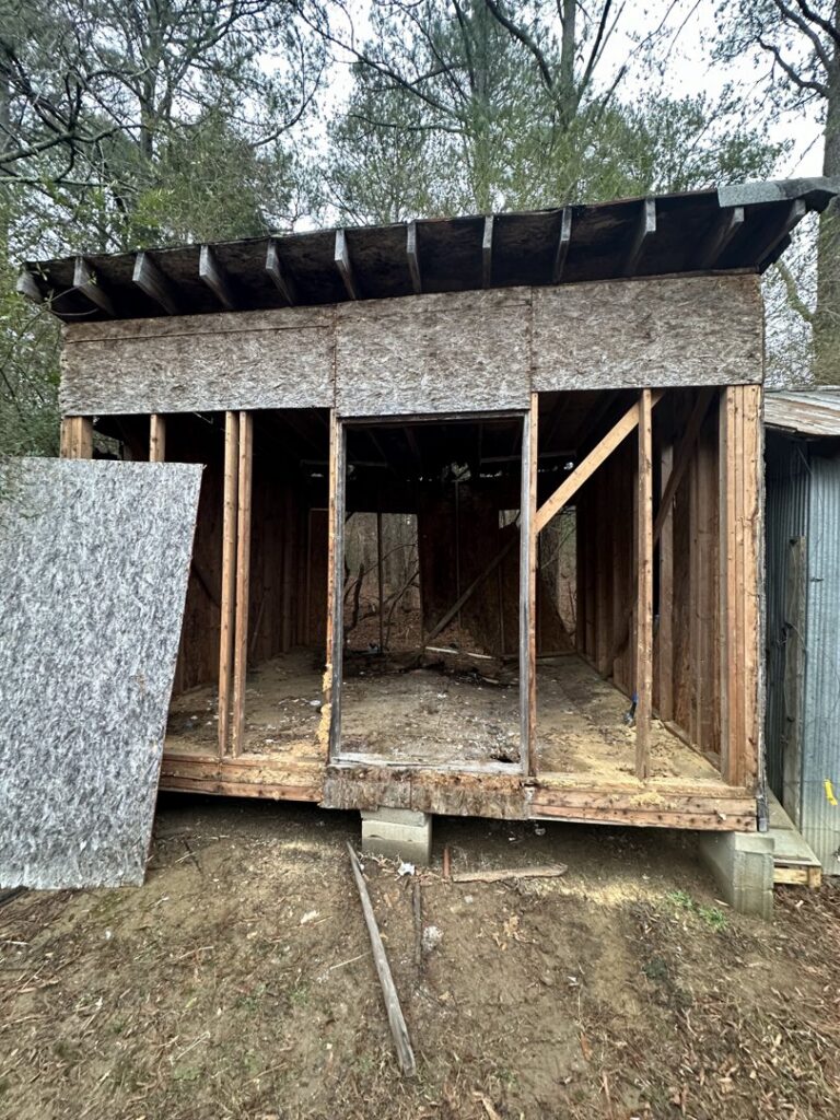 A partially demolished or repaired shed structure, showing framing and removed panels, by Ed Hauls It All in Raleigh, NC.
