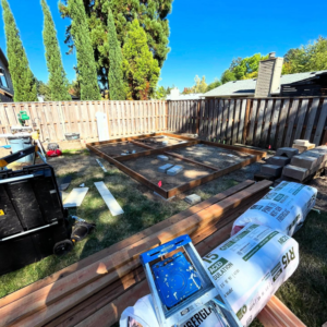A shed foundation under construction in a backyard, with lumber and insulation, by Shed Crafters in Sycamore, IL.