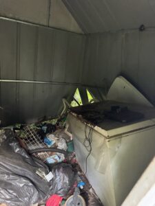 The interior of a shed filled with trash, an old freezer, and various items, indicating a shed cleanout by L.P.Z Trash & Junk Removal in Tallahassee, FL.
