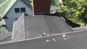 A shingle roof with a flat section, chimney, and debris, indicating a handyman cleaning or repair job by Elite Roofing Colorado Springs, CO.
