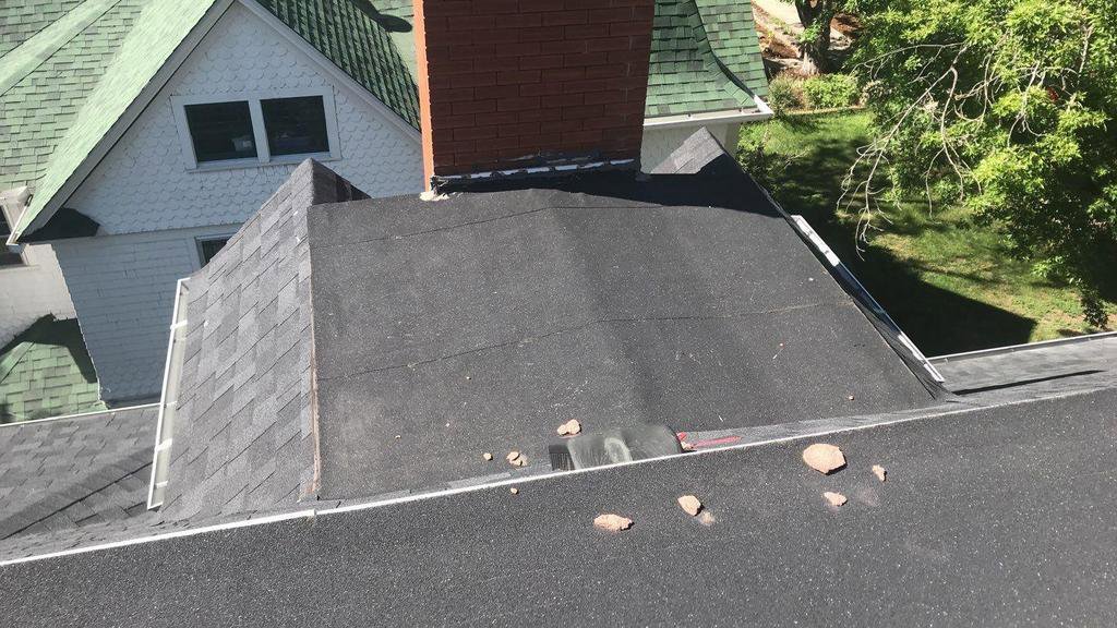 A shingle roof with a flat section, chimney, and debris, indicating a handyman cleaning or repair job by Elite Roofing Colorado Springs, CO.