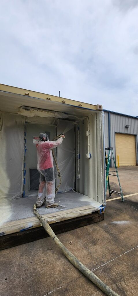 A worker applying spray foam insulation inside a shipping container for Absolute Pro Insulation in Corpus Christi, TX.