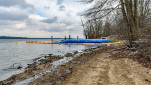 Shoreline construction with blue water barriers and yellow boom by Wilkinson Excavating, Inc. in Meadville, PA