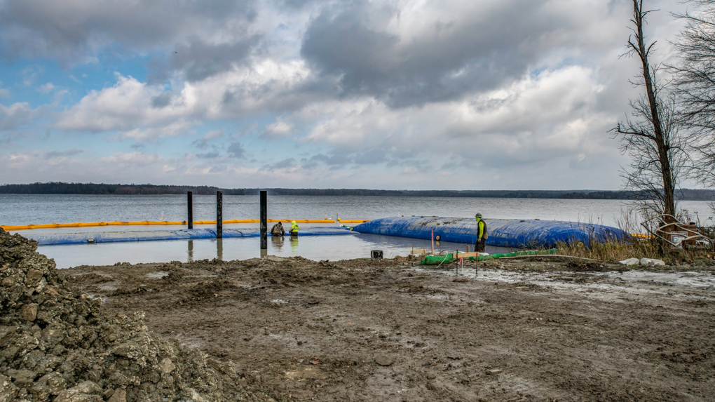 Shoreline construction project with workers and blue water barriers by Wilkinson Excavating, Inc. in Meadville, PA