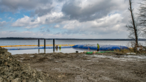 Shoreline construction project with workers and blue water barriers by Wilkinson Excavating, Inc. in Meadville, PA