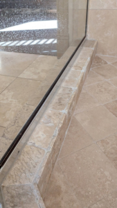 A dirty shower curb and glass door track before recaulking by SurePlan Handyman in North Ogden, UT