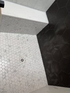 A beautifully tiled shower floor featuring white and dark hexagonal tiles, installed by Handyman Connection of Fort Collins, CO