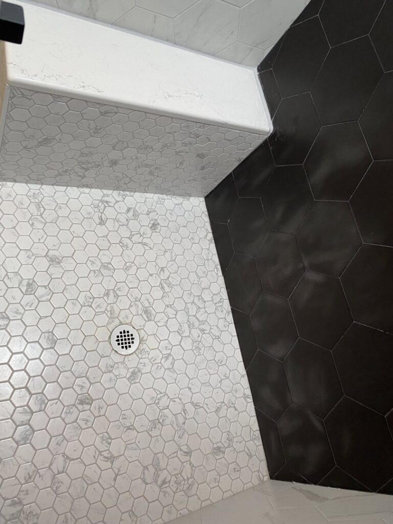 A beautifully tiled shower floor featuring white and dark hexagonal tiles, installed by Handyman Connection of Fort Collins, CO