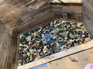 A shower floor with river rock tile installation in progress by Quality Craftsman Construction in Longwood, FL.