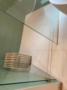 A close-up view of a shower floor with white tiles and a modern glass enclosure installed by Tess Tile By Design in Kansas City, MO.