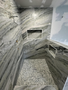 A shower with large grey marble-look wall tiles and mosaic floor tiles by A&L Tile LLC in San Diego, CA
