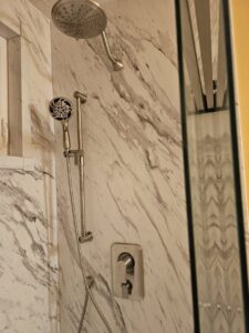 A close-up of a newly installed shower head and handheld shower on a marble-look panel by Peninsula Bath & Tile in Salisbury, MD.