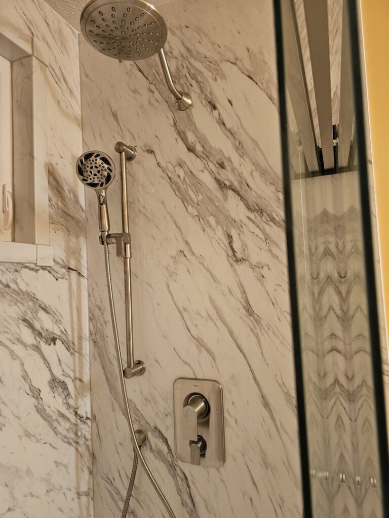 A close-up of a newly installed shower head and handheld shower on a marble-look panel by Peninsula Bath & Tile in Salisbury, MD.