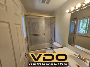A newly remodeled shower with marble-look wall tiles and a dark hexagonal floor by VDO. Remodeling in Rancho Cordova, CA.