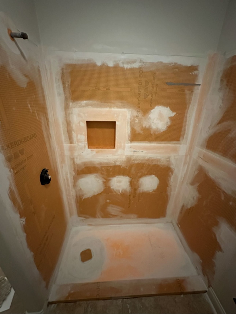 A shower enclosure under construction with waterproofing board installed by KMAC Construction in Youngsville, LA.