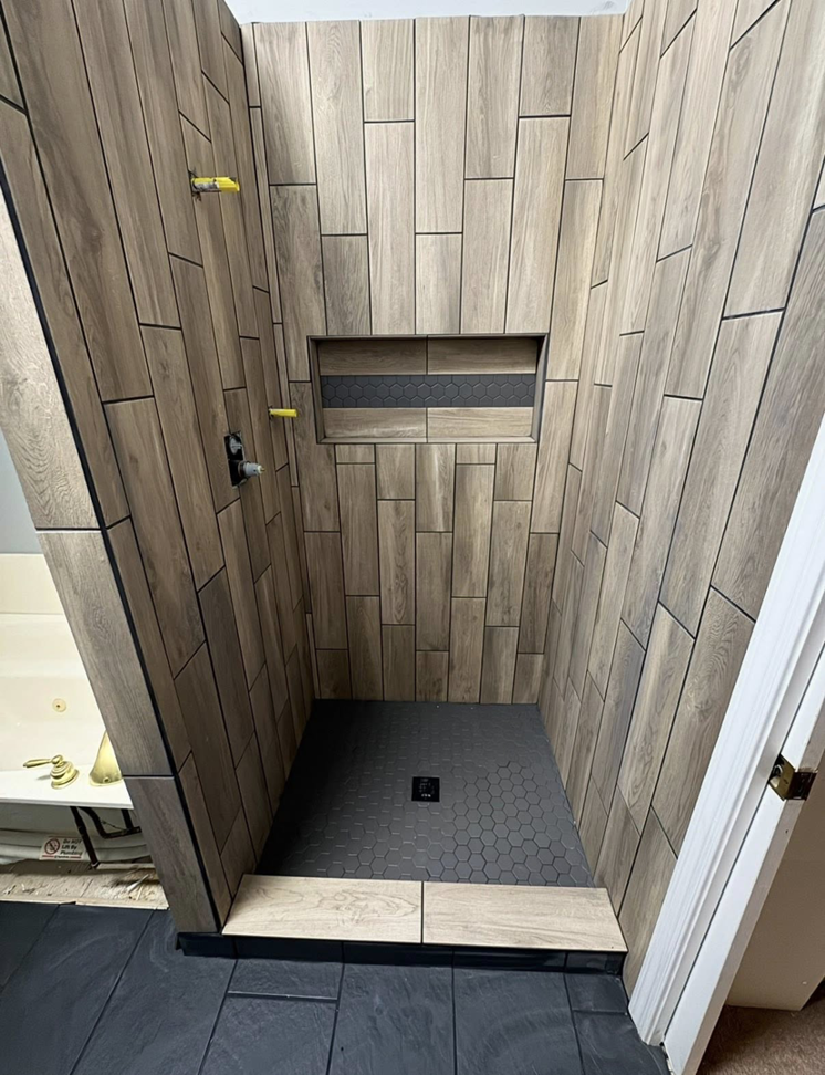 A newly tiled shower stall with wood-look wall tiles and hexagonal floor tiles by Jason Roberts Painting and Remodeling in Louisville, KY.
