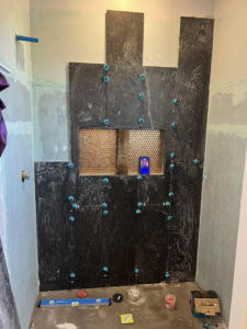 A shower wall with black tiles being installed, showing leveling clips, by HMI Contractors in Cincinnati, OH.