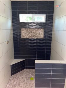 A newly tiled shower with dark blue textured tiles and a pebble floor installed by Dahlman Construction in San Tan Valley, AZ.