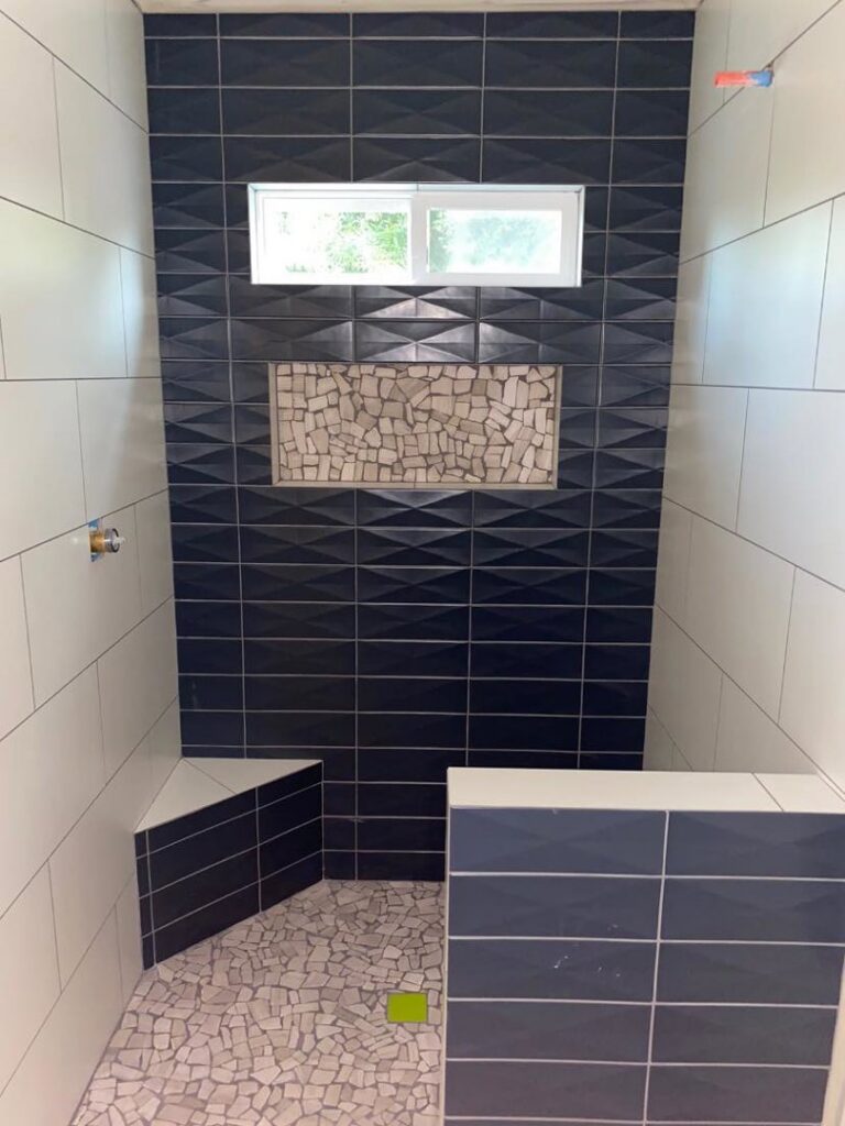 A newly tiled shower with dark blue textured tiles and a pebble floor installed by Dahlman Construction in San Tan Valley, AZ.