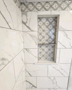 A close-up of a shower wall with a custom-built tile niche featuring decorative patterned tiles by Brian's Tiles in Duluth, MN.