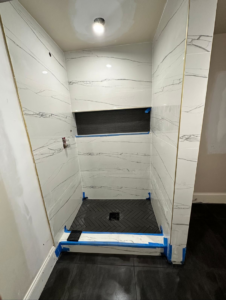 A shower tiling project in progress with marble-patterned wall tiles and black herringbone floor tiles by Home Renovation & Design in Trumbull, CT.