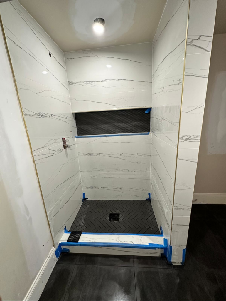 A shower tiling project in progress with marble-patterned wall tiles and black herringbone floor tiles by Home Renovation & Design in Trumbull, CT.