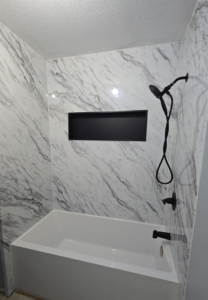 A renovated shower and tub combination featuring marble-patterned walls and black fixtures by The Shower Company in Kansas City, MO.