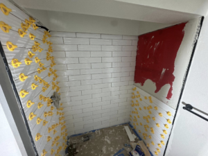 Shower walls being tiled with white subway tiles and spacers during a bathroom renovation by Peraza Handyman Services Llc in Bakersfield, CA.
