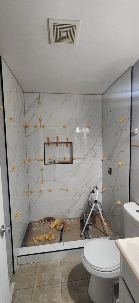 Shower walls being tiled with elegant marble-look tiles and spacers by Castillejo Handyman Services in San Diego, CA