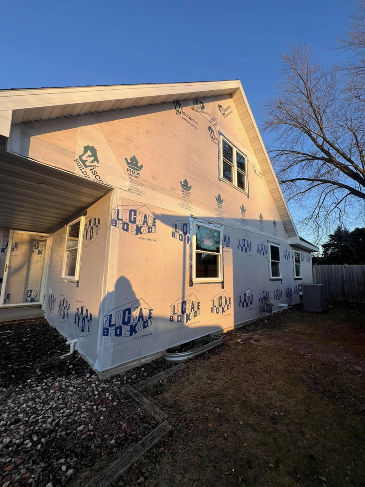 The side exterior of a house under renovation with house wrap and new windows by Sandoval Contracting & Remodeling in Menasha, WI.