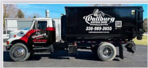 Side view of a Wallburg Disposal Worx LLC truck with a black dumpster in High Point, NC.