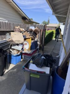 A large pile of household junk and boxes in a narrow side yard, ready for removal by Sac Junk in Rancho Cordova, CA